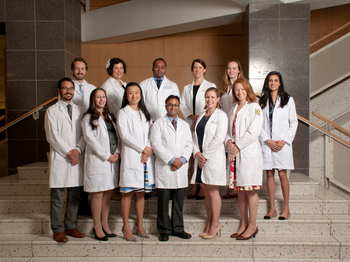 Group of graduates posing in their white coats on stairs