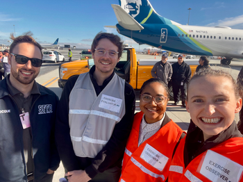 four people posing for a photo in front of an airplane
