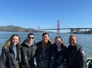 Group of people posing for a photo infront of water with a bridge in the background