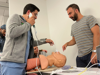 two people standing over a medical simulation head on a table