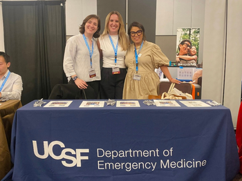 three people posing for a photo next to a UCSF table