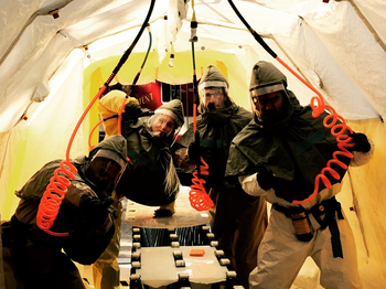 Four people in HazMat outfits in a tent with water hoses